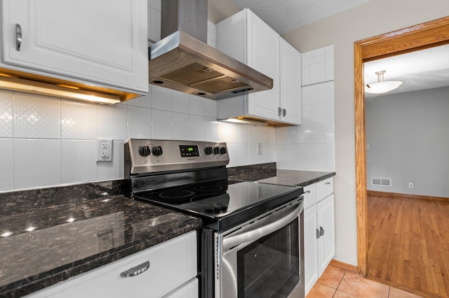 kitchen with white cabinets, decorative backsplash, wall chimney exhaust hood, and stainless steel electric range