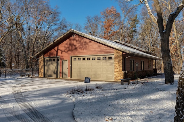 snow covered property featuring an attached garage, fence, and brick siding