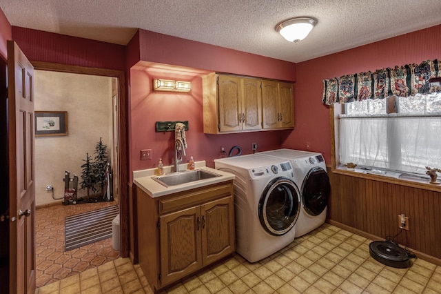 washroom featuring a textured ceiling, washing machine and clothes dryer, cabinet space, and a sink