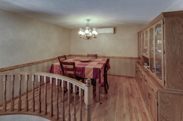 dining space with a wall mounted air conditioner, a chandelier, a textured ceiling, and light wood-style flooring