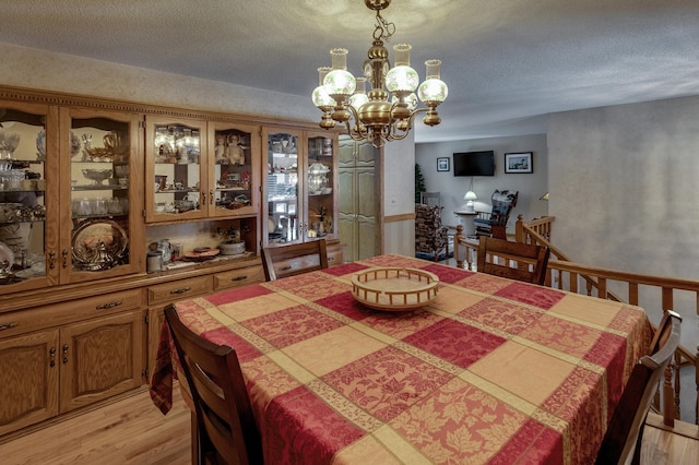 dining space featuring light wood finished floors, a notable chandelier, and a textured ceiling