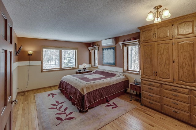 bedroom featuring a textured ceiling, a notable chandelier, light wood-style floors, and a wall unit AC