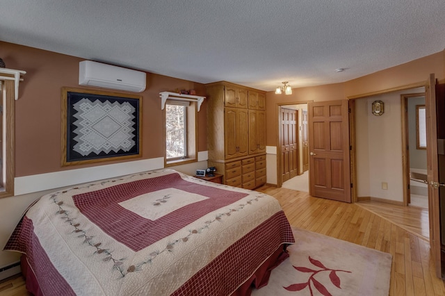 bedroom featuring baseboards, a wall mounted air conditioner, baseboard heating, light wood-style flooring, and a textured ceiling