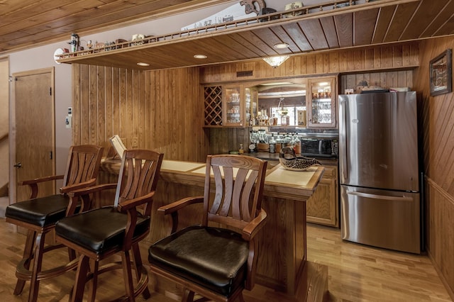 bar featuring freestanding refrigerator, indoor wet bar, wood walls, wooden ceiling, and light wood-type flooring