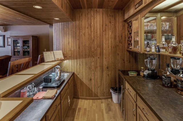 bar featuring light wood-type flooring, a bar, wood ceiling, and wooden walls