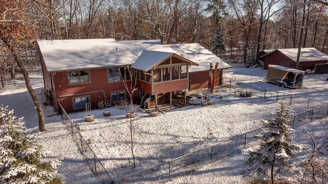 snow covered back of property with fence and a sunroom