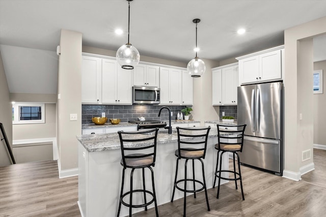 kitchen with pendant lighting, a kitchen island with sink, white cabinets, appliances with stainless steel finishes, and light hardwood / wood-style floors