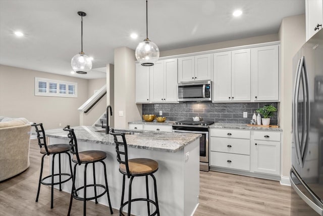 kitchen featuring white cabinets, light hardwood / wood-style floors, decorative light fixtures, and appliances with stainless steel finishes