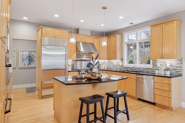 kitchen with hanging light fixtures, light wood-type flooring, light brown cabinetry, appliances with stainless steel finishes, and a kitchen island