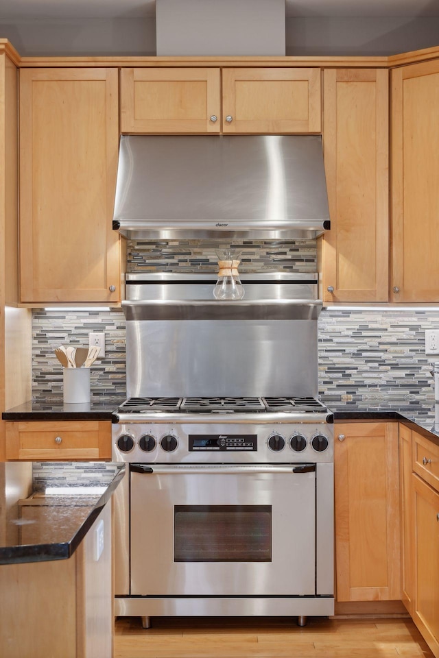 kitchen with stainless steel range, backsplash, ventilation hood, and dark stone countertops