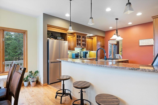 kitchen featuring light hardwood / wood-style flooring, decorative light fixtures, light stone counters, kitchen peninsula, and stainless steel refrigerator