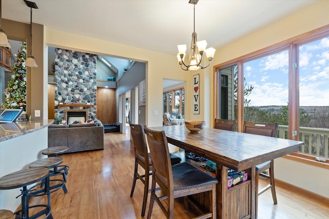 dining room with a notable chandelier, a healthy amount of sunlight, light hardwood / wood-style floors, and a fireplace