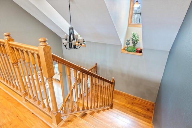 stairway featuring hardwood / wood-style flooring, vaulted ceiling, and an inviting chandelier