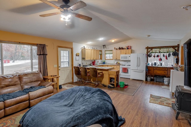 living area featuring a ceiling fan, a wood stove, vaulted ceiling, and wood finished floors