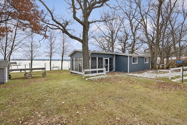 back of property featuring a lawn, a sunroom, and a water view