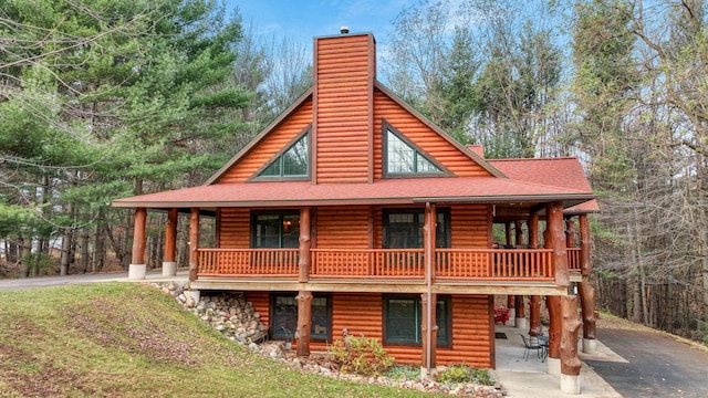 rear view of house with a chimney, a shingled roof, driveway, and a balcony