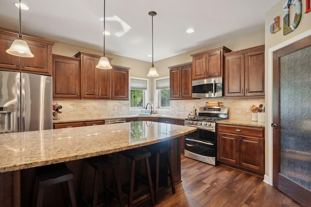 kitchen featuring a breakfast bar, hanging light fixtures, dark hardwood / wood-style floors, and appliances with stainless steel finishes