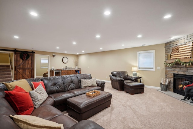 carpeted living room featuring a barn door and a stone fireplace