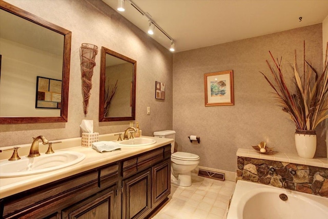 bathroom with a bath, vanity, rail lighting, and toilet