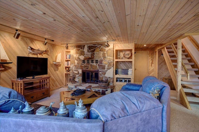 living room with carpet flooring, built in features, wooden ceiling, a stone fireplace, and wood walls