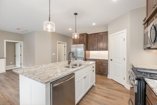 kitchen with light wood-type flooring, stainless steel appliances, a center island with sink, white cabinets, and hanging light fixtures