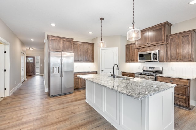 kitchen with sink, stainless steel appliances, light stone counters, a kitchen island with sink, and light wood-type flooring