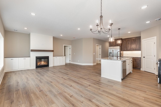 kitchen with sink, light hardwood / wood-style floors, decorative light fixtures, a center island with sink, and appliances with stainless steel finishes