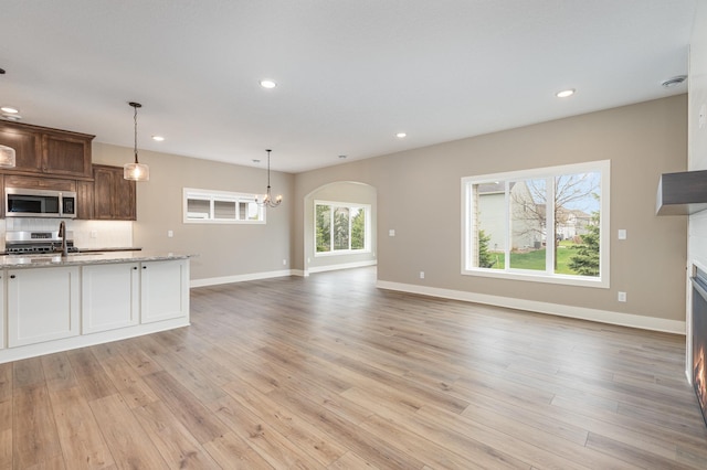 kitchen featuring light stone counters, light hardwood / wood-style floors, decorative light fixtures, and appliances with stainless steel finishes