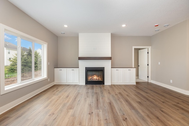 unfurnished living room featuring a textured ceiling, a large fireplace, and light hardwood / wood-style floors