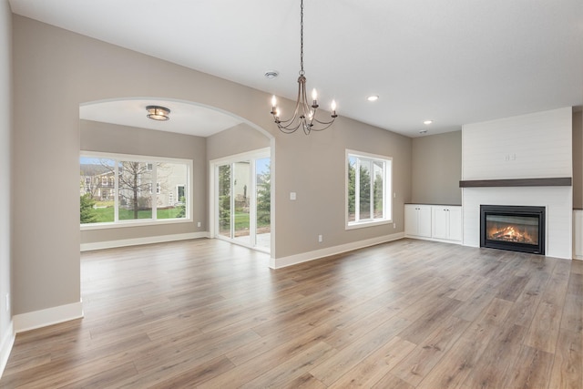 unfurnished living room featuring a fireplace, a notable chandelier, and light wood-type flooring