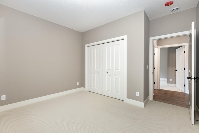 unfurnished bedroom featuring light carpet, a textured ceiling, and a closet