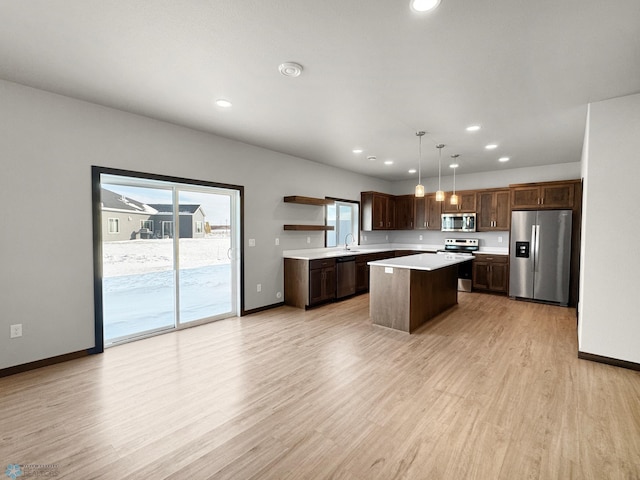 kitchen with sink, stainless steel appliances, light hardwood / wood-style floors, decorative light fixtures, and a kitchen island