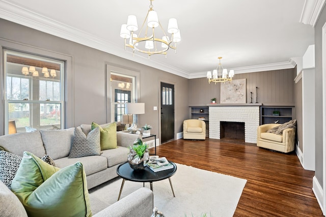 living room featuring a brick fireplace, a notable chandelier, dark hardwood / wood-style floors, and ornamental molding