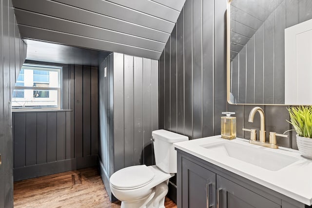 bathroom featuring toilet, wood walls, wood-type flooring, and lofted ceiling