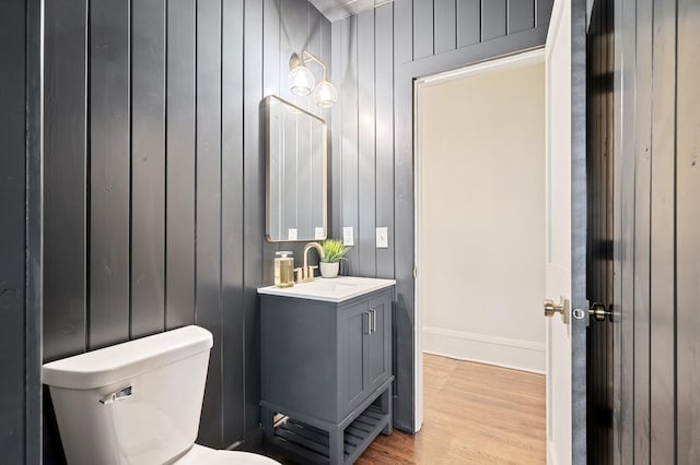 bathroom featuring vanity, toilet, wood-type flooring, and wooden walls