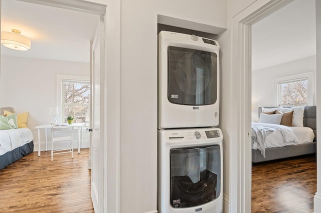 laundry area with stacked washer / dryer, a healthy amount of sunlight, and wood-type flooring