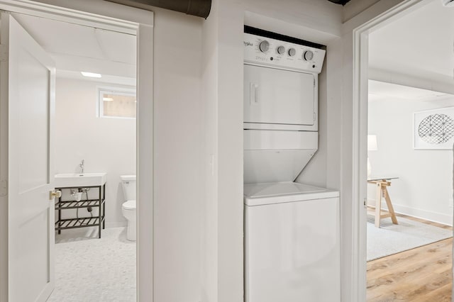 laundry area with stacked washer / drying machine, wood-type flooring, and sink