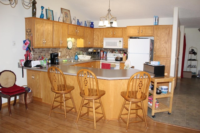 kitchen featuring kitchen peninsula, backsplash, white appliances, sink, and a notable chandelier