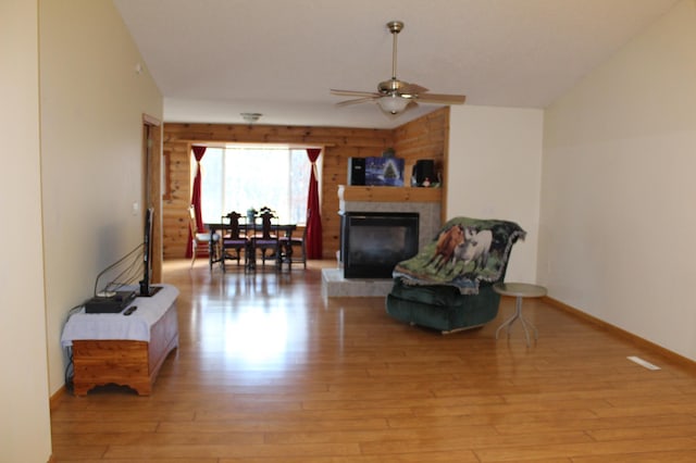 living area featuring ceiling fan, vaulted ceiling, a tiled fireplace, and light hardwood / wood-style flooring