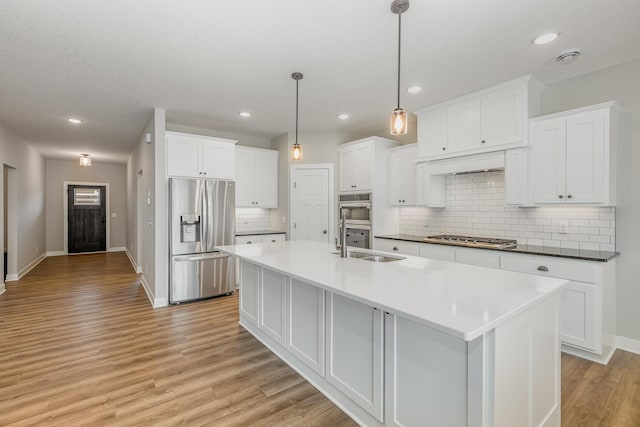 kitchen with white cabinets, appliances with stainless steel finishes, light hardwood / wood-style flooring, and pendant lighting