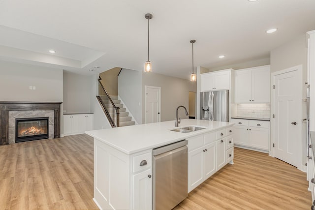 kitchen with white cabinetry, sink, stainless steel appliances, light hardwood / wood-style flooring, and a kitchen island with sink