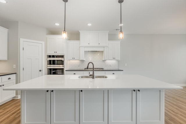 kitchen featuring an island with sink, hanging light fixtures, and light hardwood / wood-style floors