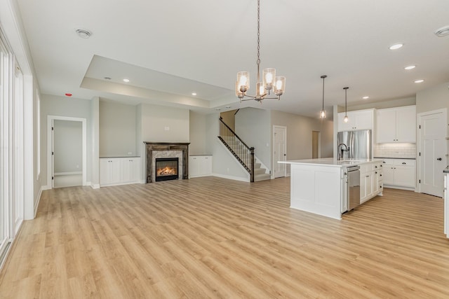 kitchen with pendant lighting, light hardwood / wood-style flooring, a fireplace, a chandelier, and an island with sink