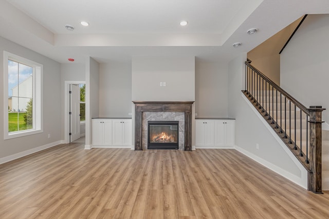 unfurnished living room featuring a tray ceiling, a fireplace, and light wood-type flooring