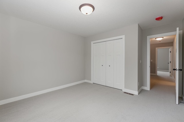 unfurnished bedroom with light colored carpet, a textured ceiling, and a closet