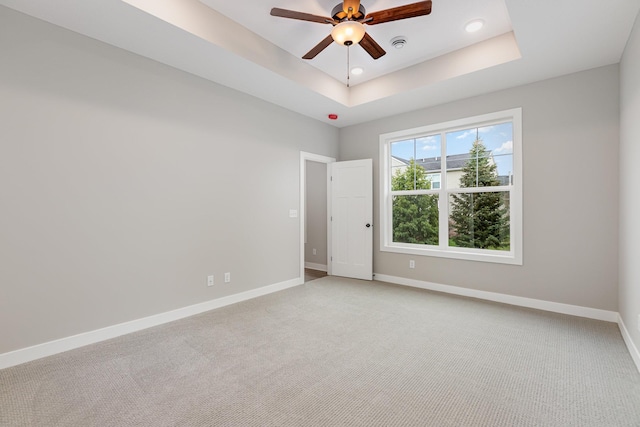 carpeted empty room featuring ceiling fan and a raised ceiling