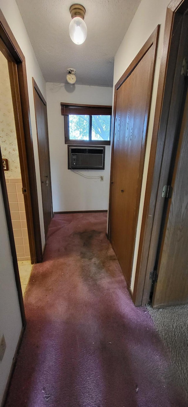 corridor with dark carpet, a textured ceiling, and a wall mounted AC