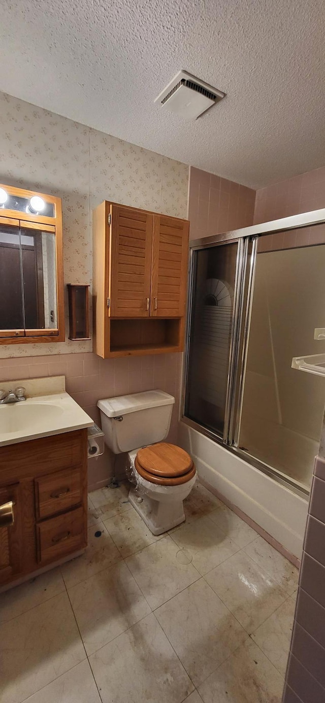 full bathroom with vanity, a textured ceiling, toilet, and shower / bath combination with glass door