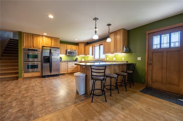 kitchen featuring a kitchen breakfast bar, light hardwood / wood-style flooring, appliances with stainless steel finishes, decorative light fixtures, and kitchen peninsula