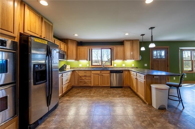 kitchen featuring kitchen peninsula, stainless steel appliances, sink, hanging light fixtures, and a breakfast bar area